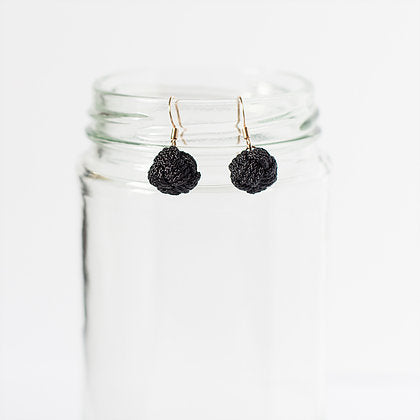 Black textured ball drop earrings displayed on a clear glass jar with a white background