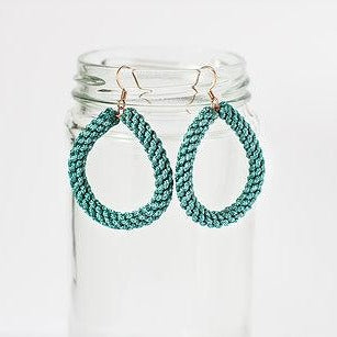 Teal woven teardrop earrings displayed on a clear glass jar, minimalist background